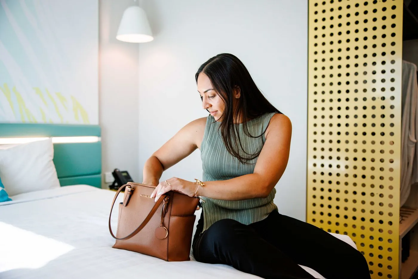 A guest sitting on the bed unpacking her handbag, the yellow perforated screen and the turquoise headboard behind her